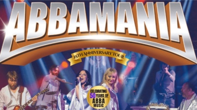 The cast of Abbamania on a brightly lit stage with the text Abbamania arching above them.